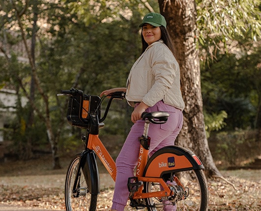 Mulher de boné verde pedalando a bike Itaú no parque.