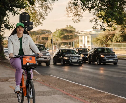 Mulher de boné verde pedalando a bike Itaú na ciclofaixa.